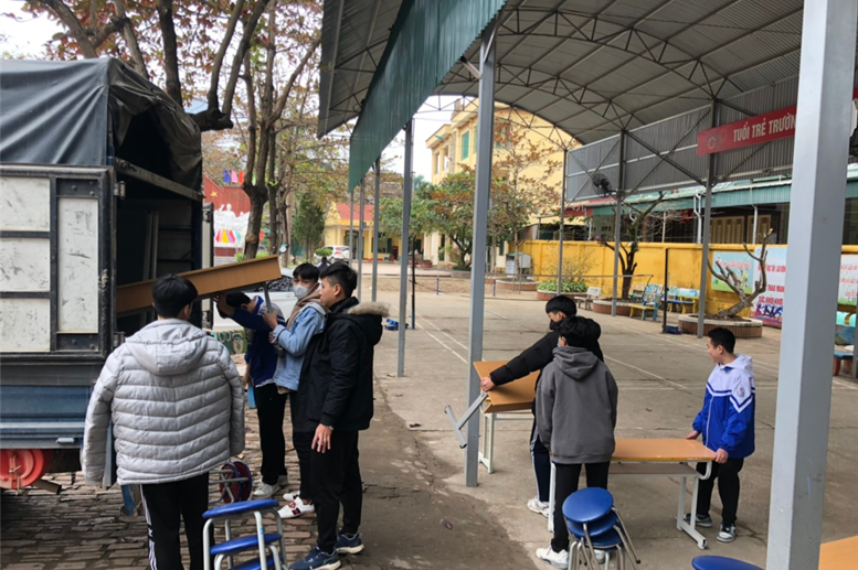 Thầy giáo Nguyễn Thành Biên và các em học sinh di chuyển bàn ghế lên xe để chở đến trung tâm.